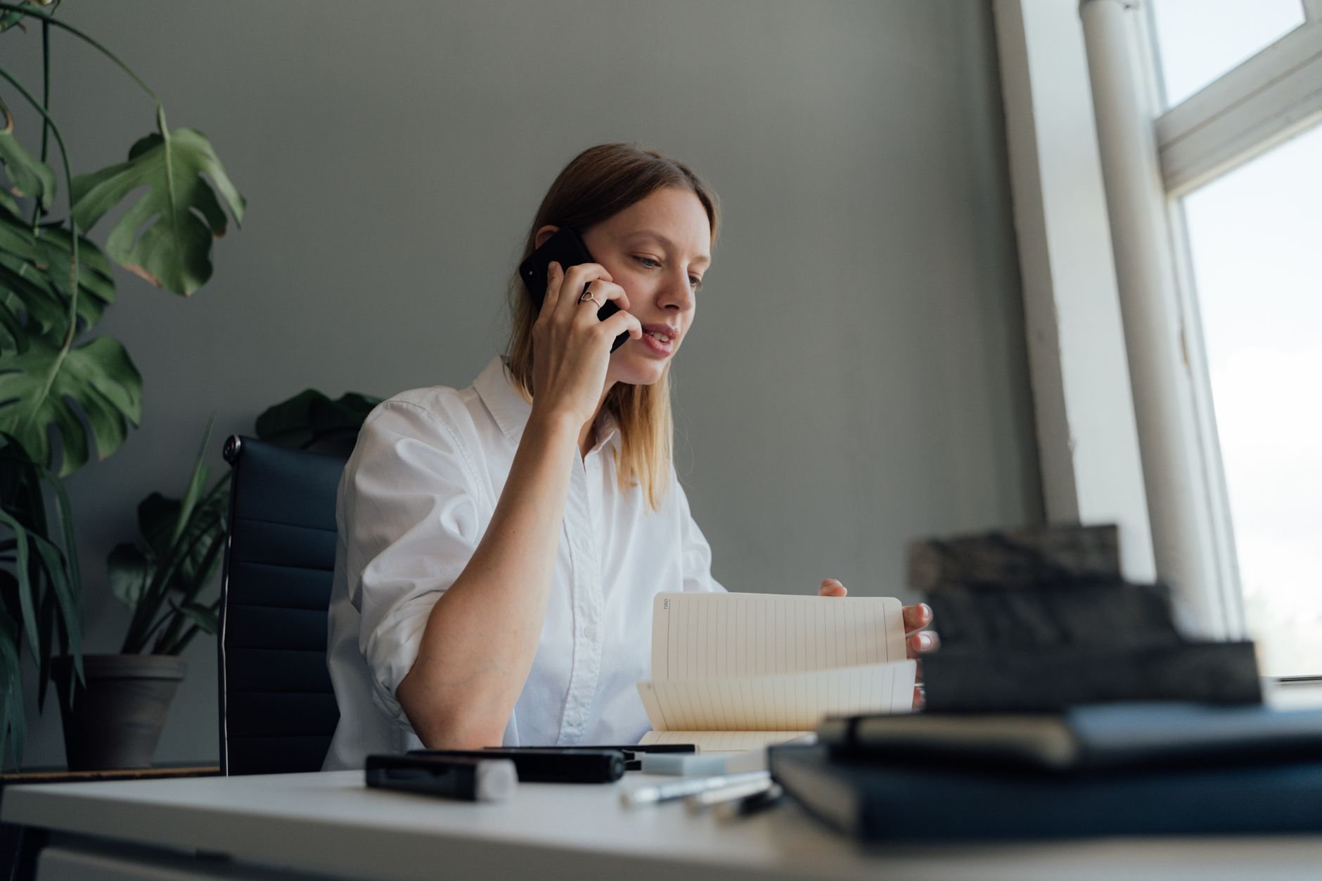 Woman on a phone call while reviewing documents at her desk indoors.